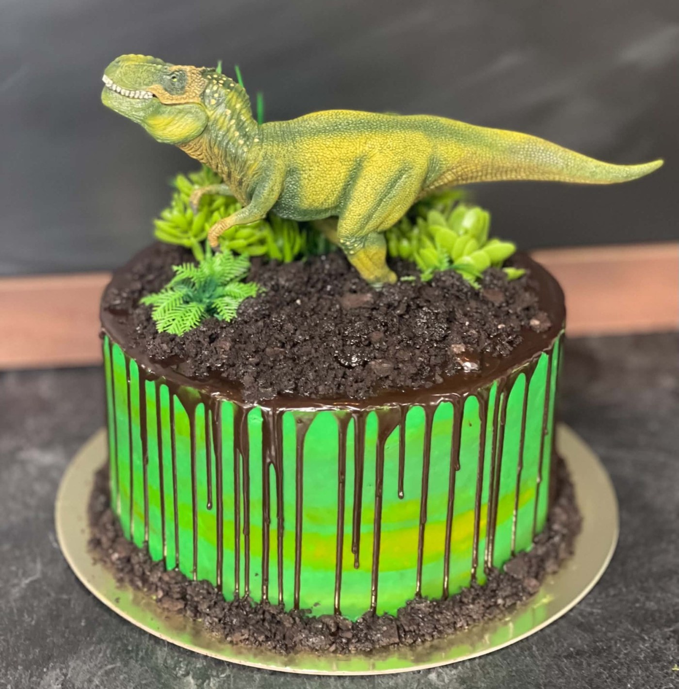 A green dinosaur-themed cake with chocolate drips